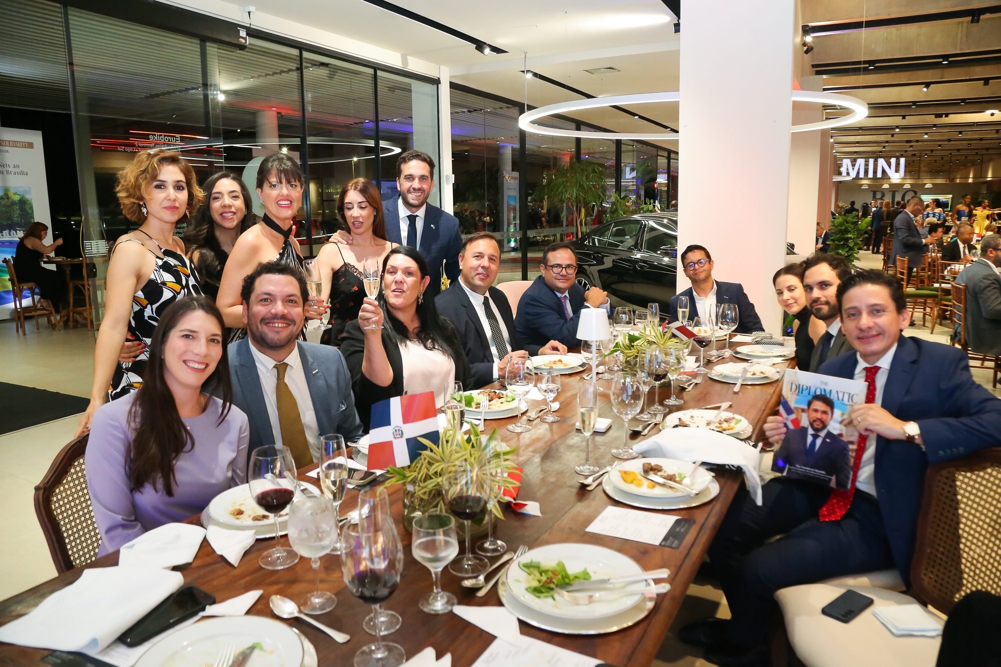 Comunidade brindando à grande mesa, com a revista e a bandeira dominicana